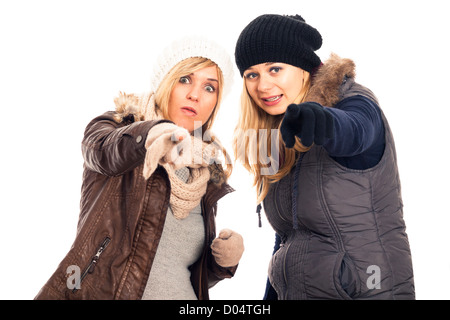 Two young surprised women in winter clothes pointing at you, isolated on white background. Stock Photo