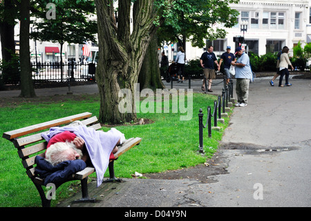 Homeless man sleeping on bench in park, Boston, Massachusetts, USA Stock Photo