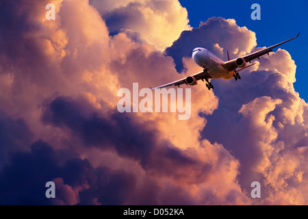 Jet plane is maneuvering for landing in a spectacular sunset sky Stock Photo