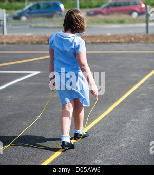 Rear view of a girl  with a skipping rope alone in the playground at a new community primary school Wales UK Stock Photo