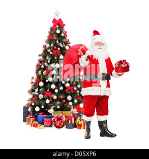Full length portrait of a Santa Claus holding a bag and standing next to a Christmas tree isolated on white background Stock Photo