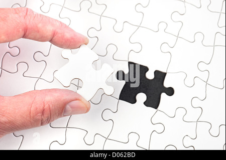 A man inserting the final puzzle piece of a white jigsaw. Stock Photo