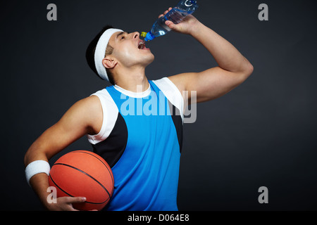 Portrait of handsome guy in sportswear with basket ball drinking water