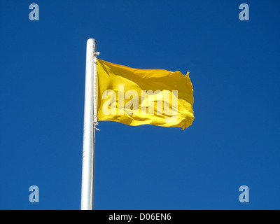 A yellow flag on the blue sky blowing in the wind Stock Photo