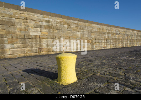 A yellow mooring bollard and sandstone block wall on the harbour at Dunbar, East Lothian, Scotland. Stock Photo