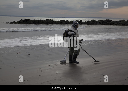 Man combs the beach at Coney Island with a metal detector in hopes that Hurricane Sandy has turned up some buried treasures. Stock Photo