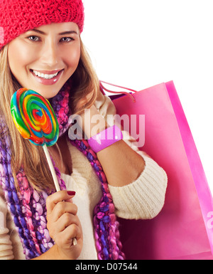 Photo of young beautiful woman lick big colorful lollipop and holding pink paper bag, pretty girl wearing red stylish hat Stock Photo