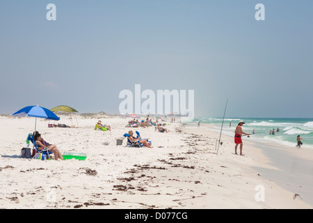 Man surf fishes while others sunbathe on white sand beach at Gulf Breeze, Florida Stock Photo