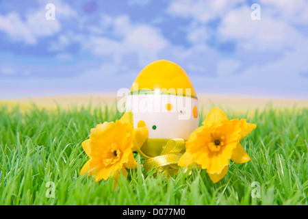plastic easter egg on grass with flowers with behind it blue sky and clouds Stock Photo