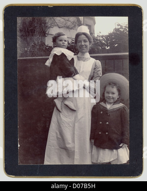 Original Edwardian cabinet card depicting a cheerful, attractive nursemaid or nursery maid with children, occupational portrait portraits   circa 1905, U.K. Stock Photo