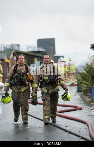 Little Warley, Essex, UK. About 5am this morning a fire started at a used cooking oil recycling plant. Massive damage was caused but no reported injuries. At the height of the blaze, Essex Fire and Rescue had 12 pumps in attendance. It was a very messy and dangerous incident for the Fire Service. Two firefighters walk away from the scene covered in grease. Stock Photo