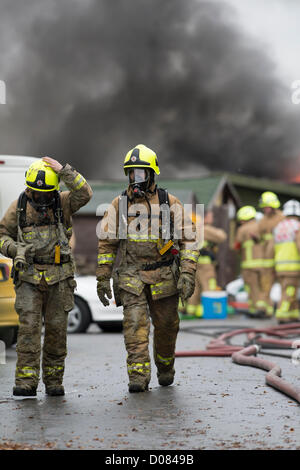 Little Warley, Essex, UK. About 5am this morning a fire started at a used cooking oil recycling plant. Massive damage was caused but no reported injuries. At the height of the blaze, Essex Fire and Rescue had 12 pumps in attendance. It was a very messy and dangerous incident for the Fire Service. Two firefighters covered in grease walk away from the scene. Stock Photo