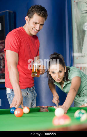 Young woman playing pool and a young man watching her game Stock Photo