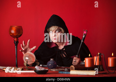 Witch holding sceptre gazes crystal ball over red background Stock Photo