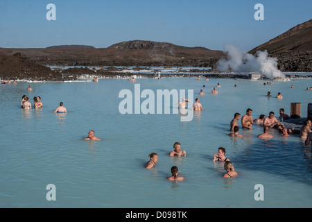 BATHERS ENJOYING HOT WATER BLUE LAGOON IN BACKGROUND SVARTSENGI GEOTHERMAL PLANT HOT SPRINGS SILICA MUD GRINDAVIK REYKJANES Stock Photo