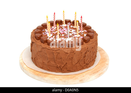 Chocolate birthday cake with candles on wooden cutting board over white background Stock Photo