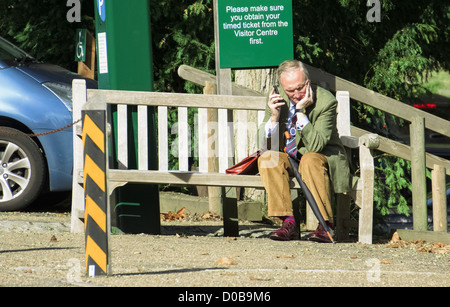A man sat on a park bench in the sun talking to someone on his mobile phone. Stock Photo