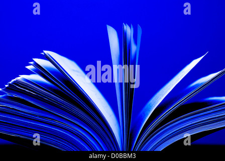 A large single book sitting with pages open on a desk and blue background Stock Photo