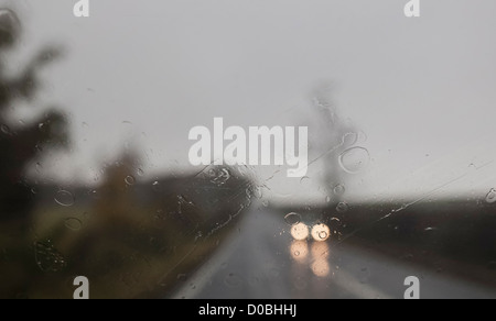 Rain on the windscreen of a car with blurred headlights approaching. Stock Photo