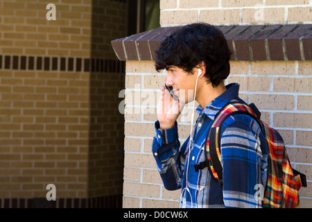 Young male college student on campus with music playing in one ear and listening on a cell phone with the other. Stock Photo
