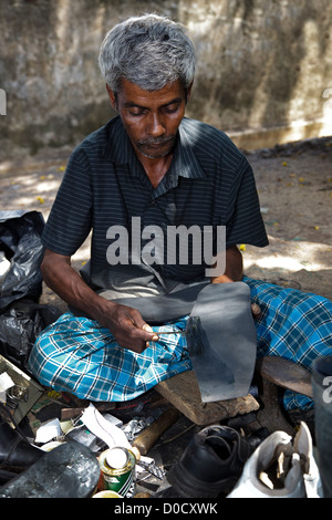 Asian man sitting on the pavement at a street market, repairing shoes and other footwear, Negombo, Sri Lanka Stock Photo