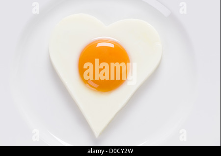 fried egg or poached egg in the shape of a heart on a white circular shaped plate. Egg presented soft 'sunny side up' 'eggs up' Stock Photo