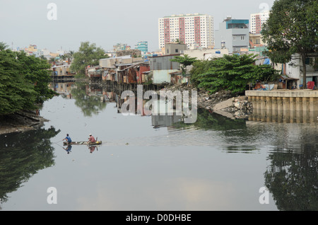 HANOI, Vietnam — Two men in a small wooden canoe use a net to fish in the still waters of a tributary of the Saigon River in Ho Chi Minh City, Hanoi, with makeshift houses on the waterfront and tall highrises in the background. Stock Photo