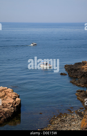 View of rocky cove and small motor boats at mountainous Kullaberg near Mölle in south-west Sweden. Scuba divers on one with diver' flag. Stock Photo