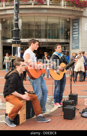 Typical street scene with three Irish musicians young men playing guitars busking in city centre on Grafton Street Dublin Eire Ireland Stock Photo