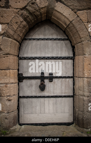 Caernarfon Castle Arched Doorway Caernarfon Wales / CAERNARFON, Wales — A stone arched doorway within Caernarfon Castle in northwest Wales. The medieval fortress was commissioned by King Edward I in the summer of 1283, replacing a Norman motte-and-bailey from the late 11th century on the same site, with construction under Master James of St George continuing until around 1330. The widespread use of the shouldered corbelled lintel throughout the castle gave its name to the architectural term "Caernarfon arch." The castle's distinctive polygonal towers and massive masonry walls — curtain walls u Stock Photo