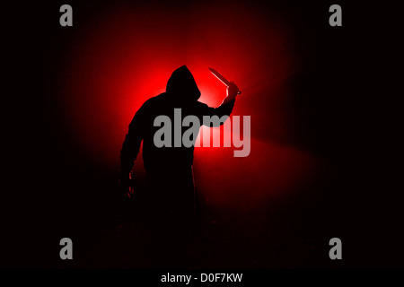 Psycho Killer - Knife: Dark, foggy outdoor silhouette of a man wearing a hooded sweatshirt, weilding a large knife. Stock Photo