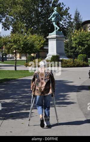 A woman on crutches walks in a park toward a war memorial, Ontario, Canada Stock Photo