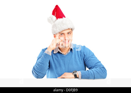 A smiling male wearing a santa hat and posing behind a blank panel isolated on white background Stock Photo