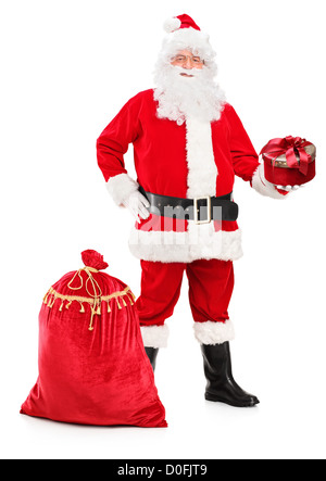 Full length portrait of a Santa Claus holding a gift and bag full of presents next to him isolated on white background Stock Photo