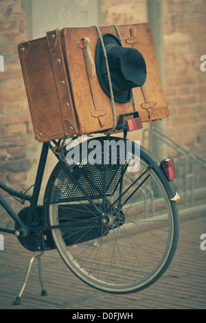 Shabby black hat and brown suitcase on old bike. Retro-style toned image Stock Photo