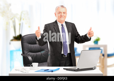 Happy mature businessman standing in his office and giving thumbs up Stock Photo