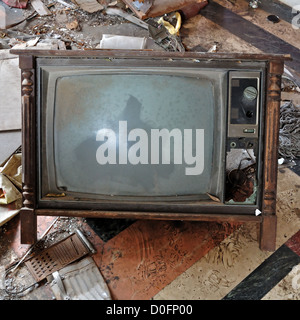 Vintage broken television tv set with wooden frame on dirty floor. Stock Photo