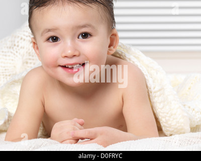 Portrait of a cute smiling two year old baby boy lying on a bed under a blanket