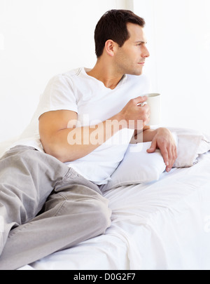 Handsome young man reclining on his bed with a cup of coffee Stock Photo
