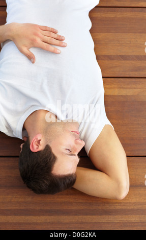 Young, male lying on a wooden floor; his mind a million miles away Stock Photo