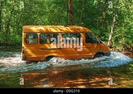 Yellow minibus fording small river. Stock Photo