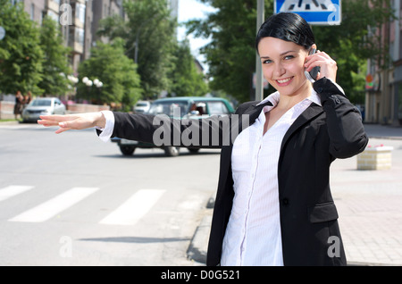 Beautiful young businesswoman hailing taxi cab using cell phone Stock Photo