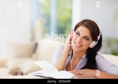 An attractive young woman listening to her headphones while reading Stock Photo