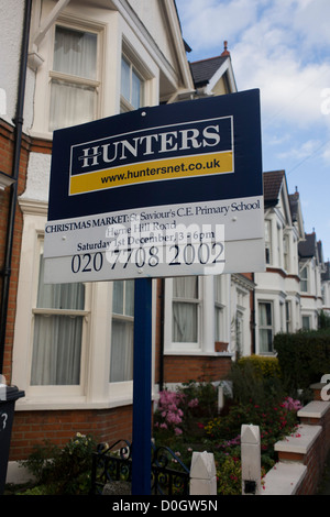 Local London Estate Agent Hunters, advertises a school Chrostmas fete with a mention on their housing placard.  Looking upwards to the sign, we see beyond and stretching into the distance a row of Victorian terraced homes in the south London suburb of Herne Hill, Lambeth SE24, approximately 5 miles south of the river Thames. As a piece of local PR, the company likes to be viewed as helping the neighbourhood by sponsoring events such as this Christmas market in the nearby school. Stock Photo