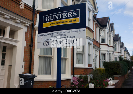Local London Estate Agent Hunters, advertises a school Chrostmas fete with a mention on their housing placard.  Looking upwards to the sign, we see beyond and stretching into the distance a row of Victorian terraced homes in the south London suburb of Herne Hill, Lambeth SE24, approximately 5 miles south of the river Thames. As a piece of local PR, the company likes to be viewed as helping the neighbourhood by sponsoring events such as this Christmas market in the nearby school. Stock Photo