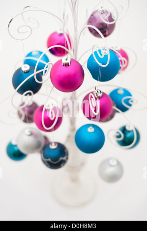 Brightly coloured Christmas baubles hanging from a decorative white metal stand Stock Photo