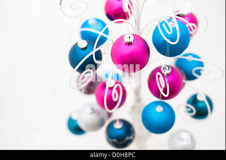 Brightly coloured Christmas baubles hanging from a decorative white metal stand Stock Photo