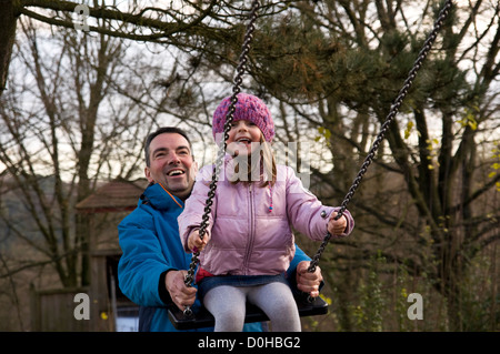 Smiling father pushing daughter on a swing in a park, Germany Stock Photo