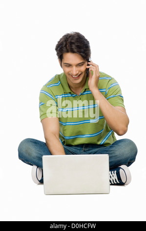 Young man using a laptop and talking on a mobile phone Stock Photo