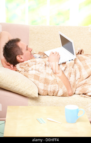 Man with cold laying on sofa with laptop, his medicines on the tablet Stock Photo